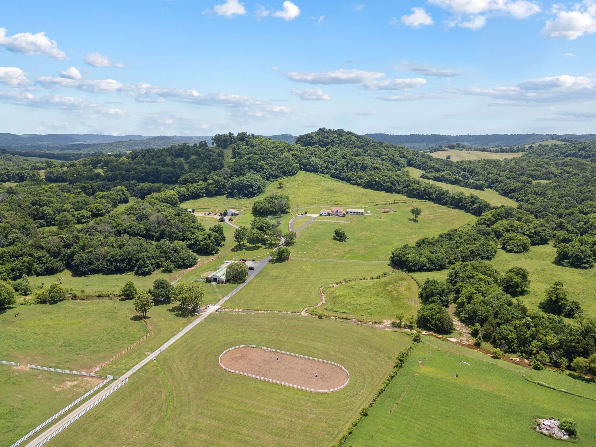 Wide aerial of the property — round pen, white-fenced paddocks, farmhouse on the hill, rolling hills beyond