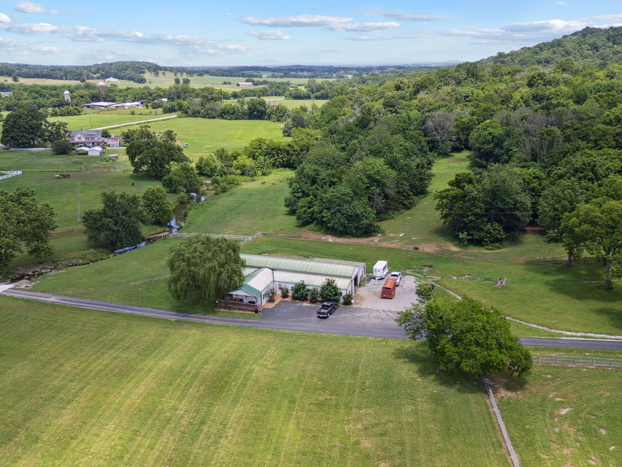 Aerial of the barn and willow with horses grazing in the distance and a creek winding through the valley