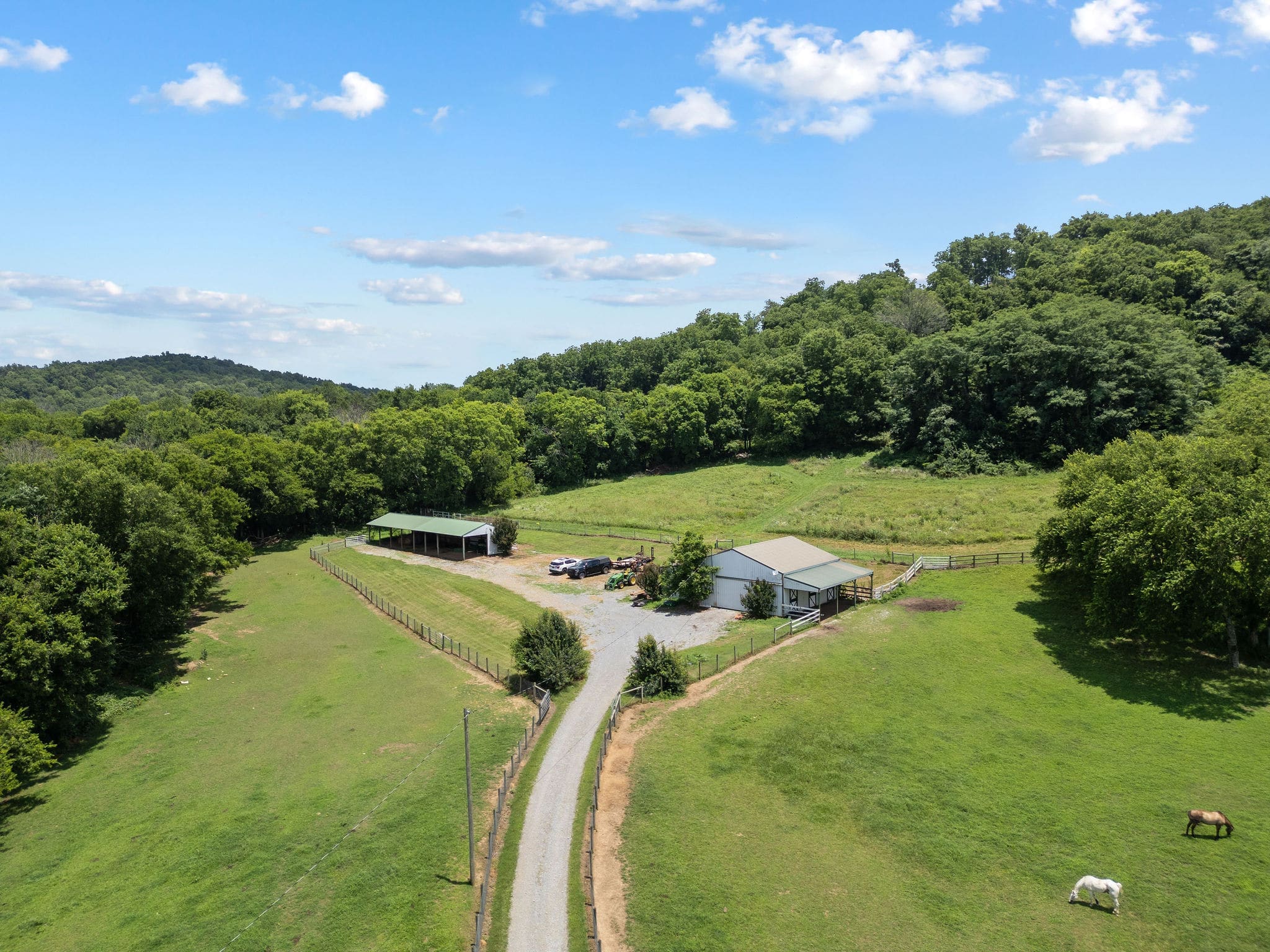 Aerial of the barn complex with two horses grazing in the foreground and the gravel drive curving in