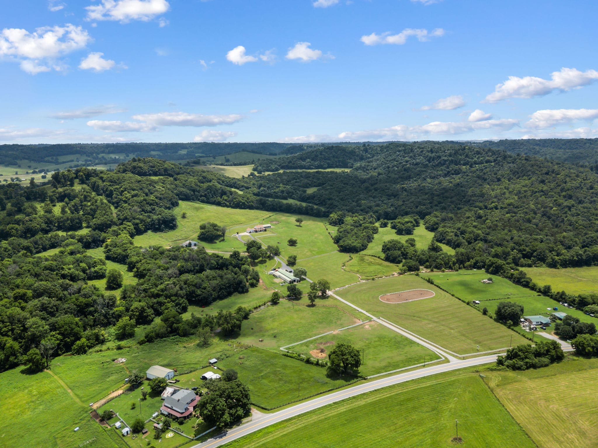 A sweeping aerial of the whole property — barn complex, round pen, white-fenced paddocks, and the valley beyond