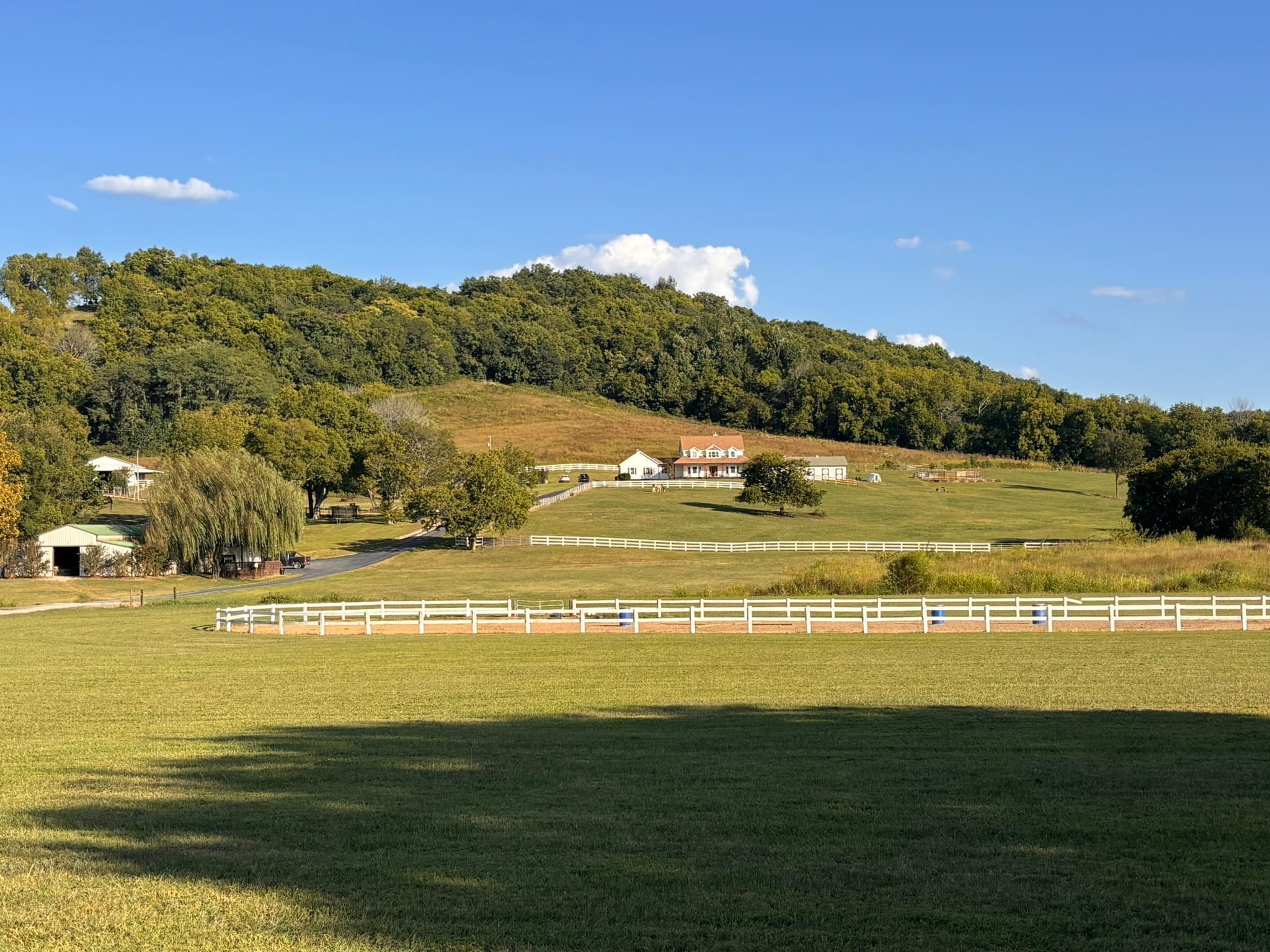 Wide view of the farmhouse, paddocks, and white fencing on a clear day
